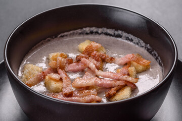 Fresh delicious hot puree soup with mushrooms and bacon in a black plate