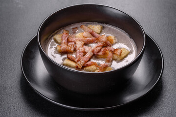 Fresh delicious hot puree soup with mushrooms and bacon in a black plate