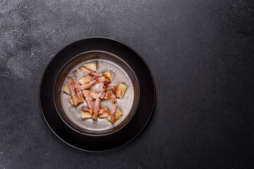 Fresh delicious hot puree soup with mushrooms and bacon in a black plate
