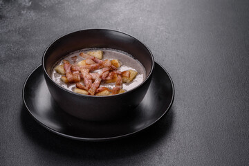 Fresh delicious hot puree soup with mushrooms and bacon in a black plate