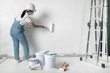 girl paints a white wall with a roller. Repair of the interior. Young female decorator painting a...