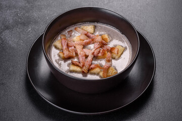 Fresh delicious hot puree soup with mushrooms and bacon in a black plate