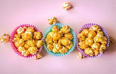 Sweet caramel popcorn in a colorful cups on a pink background
