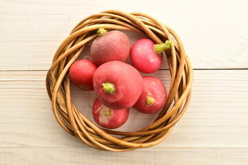 Organic ripe, light red radish with a vine wreath, close-up, on a wooden table.