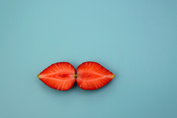 Juicy fresh strawberries, split into two halves on a blue background.