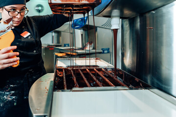 professional female chocolatier working at the confectionery workshop with a machine. Chocolate...