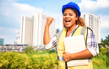 Portrait of woman architect standing with laptop for construction plan in the public park. Back view of contractor on background of modern office buildings with blue sky.