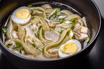 Fresh delicious hot soup with noodles and quail egg in a black plate