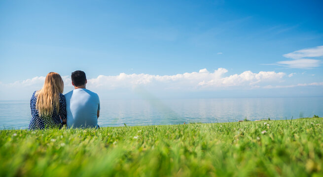 A young couple in love is sitting nearby on a green lawn on the background of an endless blue sky