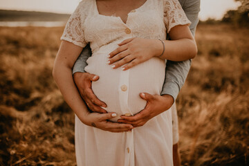 hands of future mother and father clasped pregnant big tummy.