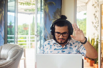 Young Latino male college student with headset, raising his hand in class in virtual classroom in...
