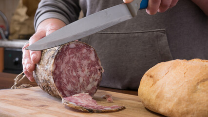closeup of italian sopressa salami with homemade bread with knife and being cut