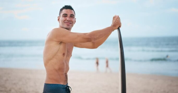 Brazilian surfer stands with surf board on the beach looks into the camera and smiles