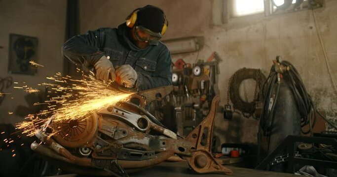 Locksmith sands the decorative metal steampunk fish sculpture by electric grinder with a lot of sparks in slow motion, metalwork at workshop, 4k 60p Prores HQ