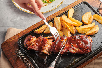 manos de mujer  partiendo costillas bbq sobre una mesa gris con papas y ensalada