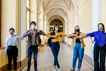 Group of five people friends in facial masks bump their elbows instead of greeting of greeting with a hug in learn time indoor. Avoid the spread of coronavirus, social distance and friendship concept.