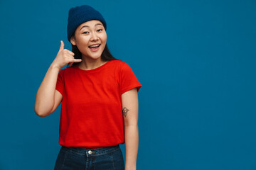 Asian teen girl in hat smiling and showing handset gesture