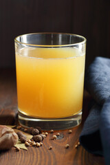 Bone collagen broth or soup in glass on wooden table on dark moody rustic background with spices and blue linen napkin nearby, closeup, vertical, liquid diet, paleo diet, collagen food concept