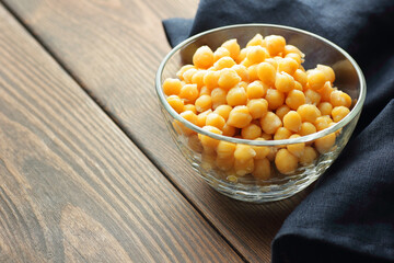 Boiled chickpeas in a glass bowl on rustic wooden table with blue cloth nearby, closeup, copy space, lenten fasting food, vegan protein meal concept