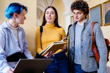 Student life un high school. Three students people talking together in university hall. Brunette...