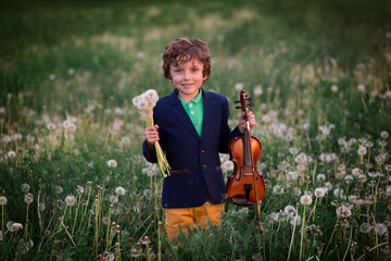 Curly-haired talented boy plays the violin in nature at sunset