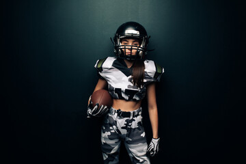 Fototapeta na wymiar Athletic woman poses in American football uniform and helmet with ball.