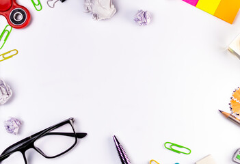 Waste paper crumbs, fidget spinner, eye glasses, ball pen, pencil and sticky notes shot from top against white background.