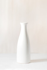 One white vase on a white table. In the background there is a light milky background.