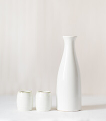 White vase and two white glasses on a white table. In the background is a light milky background.