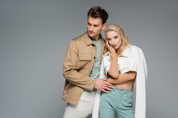 trendy models in pants and jackets posing isolated on grey