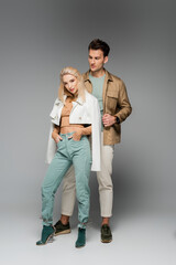 full length of model in jacket posing with hands in pockets near man on grey