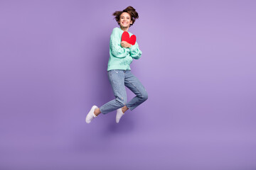 Fototapeta na wymiar Full length body size view of attractive cheerful amorous girl jumping hugging heart card isolated over violet purple color background