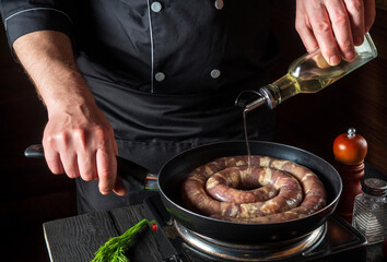 The chef adds oil to pan with raw meat sausage. Preparation for cooking sausages in the kitchen of a restaurant or cafe on table with vegetables