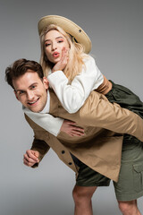 positive man piggybacking cheerful blonde woman isolated on grey