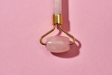Close up shot of Rose quartz facial massage roller isolated over pink background