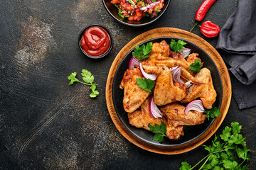 Grilled chicken wings or roasted bbq with spices and tomato salsa sauce on a black plate. Top view with copy space.