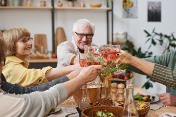 Group of old friends toasting with glasses of red wine while sitting at dining table