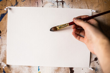 Mockup. Brush for painting in the hand of a man on a background of a white sheet of watercolor...