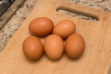 Five fresh brown organic eggs sitting out on a wooden cutting board