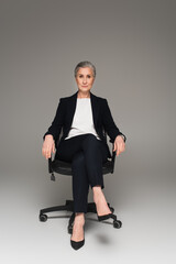 Mature businesswoman looking at camera on office chair on grey background