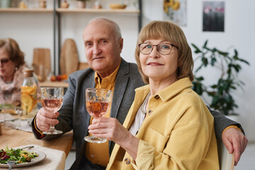 Portrait of senior couple looking at camera while sitting at dining table and drinking wine during dinner