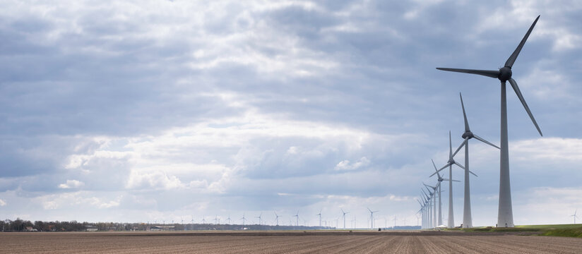 Wind farm with windmills along the dike on the coast of the IJsselmeer in the Noordoostpolder with a beautiful cloudy sky. Wide picture