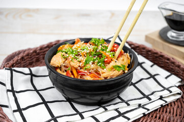 Asian salad with rice noodles, vegetables, mushrooms, chicken and soy sauce. Funchose with white transparent noodles in black plate