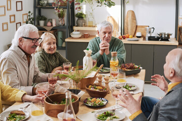 Senior people sitting at dining table and talking to each other during dinner at home