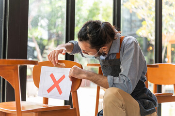 Asian waiter attach marks cross sign on the chair in the restaurant or cafe to make social...