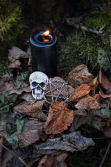 Black candle, Human skull occult amulet, pentagram in dark mystical autumn forest. Black magic...