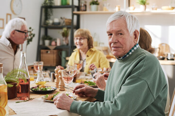 Portrait of senior man looking at camera while having dinner with his friends at the table