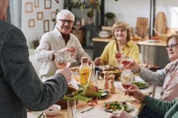 Man holding glass of red wine and saying the toast while other people listening to him at the table