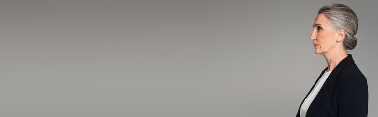 Side view of grey haired businesswoman standing isolated on grey, banner
