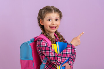 A little smiling girl points her finger at your ad on a pink isolated background.